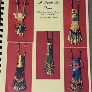 May include: A book cover titled A Bead In Time Miniature Charm Purses Objects of Arte by Lisa Ann Claver, featuring five photographs of intricate, colorful beaded miniature purses with long fringe and decorative charms hanging from beaded necklaces.