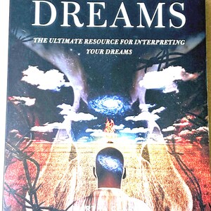 May include: A book titled "The Big Dictionary of Dreams" with the subtitle "The Ultimate Resource for Interpreting Your Dreams." The cover features a surreal illustration of a person with a galaxy in their head, a fiery element, and a landscape.