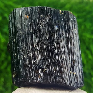 May include: A black tourmaline crystal with a striated surface. The crystal is raw and unpolished, with a natural, rough texture.