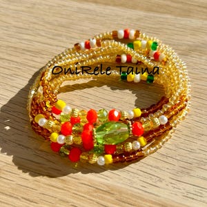 May include: A multi-strand beaded bracelet with a green, red and yellow colour scheme. The bracelet features a large green bead in the centre and smaller beads in various colours throughout. The bracelet is on a wooden surface.