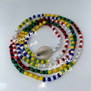 Op de afbeelding: Een kleurrijke kralen armband met een schelpbedel. De armband is gemaakt met rode, gele, groene, blauwe en witte kralen. De tekst "OniRere Taina" staat op de armband.