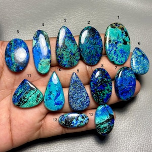 May include: Thirteen polished azurite-malachite cabochons in various shapes, including oval, pear, and teardrop, displaying vibrant blue and green mineral patterns. Each stone is numbered from one to thirteen, showcasing unique colour variations.