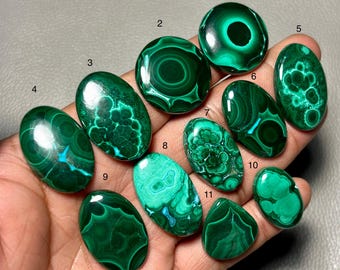 Pode incluir: Uma coleção de onze pedras preciosas de malaquite polidas em várias formas, incluindo ovais, redondas e em forma de gota. As pedras exibem uma rica cor verde com intrincados padrões de redemoinho e alguns detalhes em turquesa. As pedras preciosas são exibidas em uma superfície neutra.
