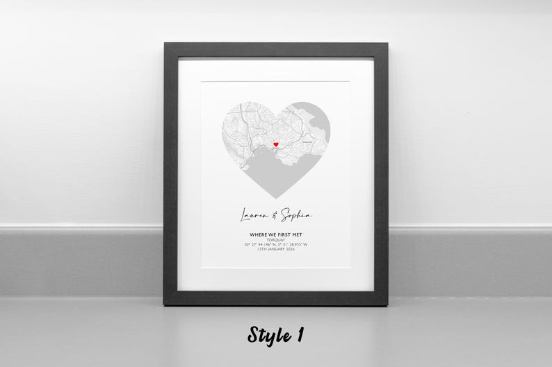 May include: A framed print featuring a heart-shaped map with a red heart icon marking a specific location. Below the map, the text reads: Lauren & Sophia, WHERE WE FIRST MET, TORQUAY, 50 27' 44.146" N, 3 31' 38.925" W, 12TH JANUARY 2024.