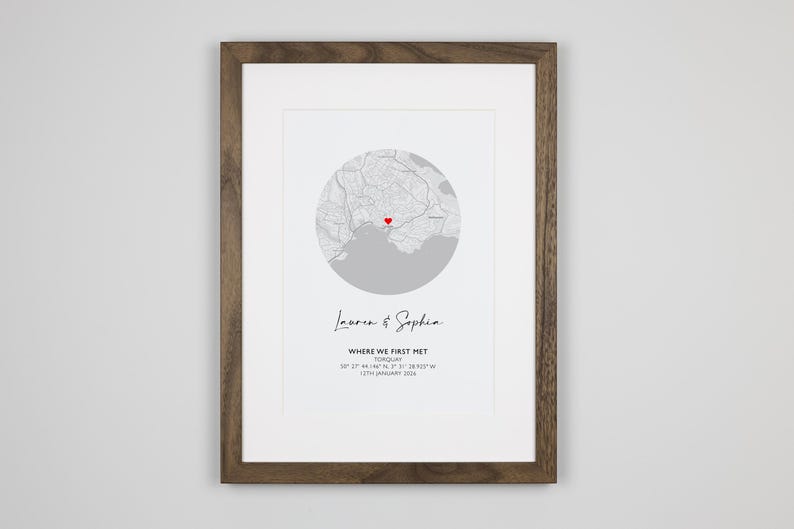 May include: A framed print featuring a circular grey map with a red heart icon marking a specific location. Below the map, the text reads Lauren & Sophia, WHERE WE FIRST MET, TORQUAY, 50 27 44.146 N, 3 31 28.825 W, 12TH JANUARY 2016.