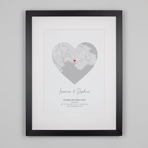 May include: A framed print featuring a gray map shaped like a heart with a small red heart icon at the center. Below the map, the text reads: Lauren & Sophia, WHERE WE FIRST MET, TORQUAY, 50&deg; 27' 44.146" N, 3&deg; 31' 28.925" W, 17TH JANUARY 2020.