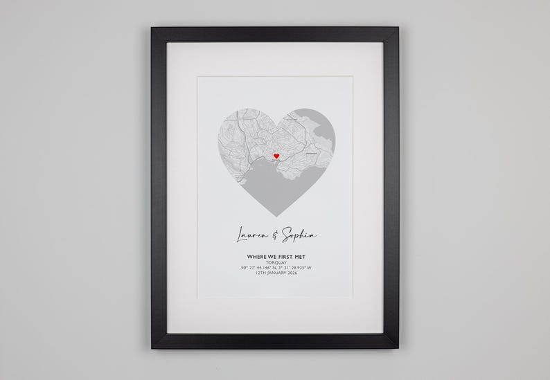 May include: A framed print featuring a gray map shaped like a heart with a small red heart icon at the center. Below the map, the text reads: Lauren & Sophia, WHERE WE FIRST MET, TORQUAY, 50&deg; 27' 44.146" N, 3&deg; 31' 28.925" W, 17TH JANUARY 2020.