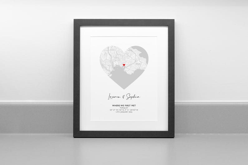May include: A framed print featuring a heart-shaped map of Torquay with a small red heart icon marking a specific location. Below the map, the text reads Lauren & Sophia, WHERE WE FIRST MET, TORQUAY, 50 27' 44.146" N, 3 31' 38.923" W, 12TH JANUARY 2024.