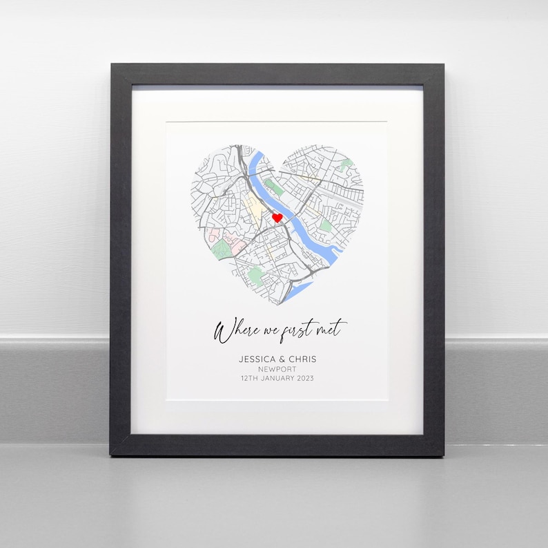 May include: Framed print featuring a heart-shaped map with a red heart marking a location. The text "Where we first met" is above the names Jessica & Chris, and the date 12th January 2023.