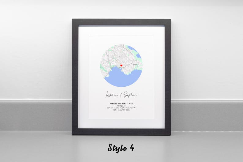May include: A framed wall art print featuring a circular map of Torquay with a red heart icon. Below the map, the text reads Lauren & Sophia, WHERE WE FIRST MET, TORQUAY, 50 27' 44.148" N, 3 31' 18.923" W, 17TH JANUARY 2016. The frame is black.