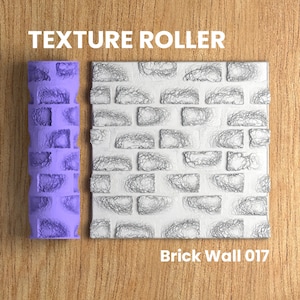 May include: A purple texture roller with a brick wall pattern. The roller is next to a sample of the pattern, which is a white brick wall with a textured surface. The text "Brick Wall 017" is below the sample.