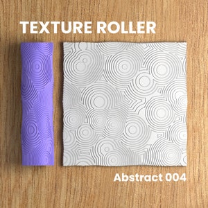 May include: A purple texture roller with a repeating pattern of concentric circles. The roller is used to create a textured surface on a material. The image also shows a sample of the texture created by the roller, which is a white surface with a repeating pattern of concentric circles. The text "Abstract 004" is below the sample.