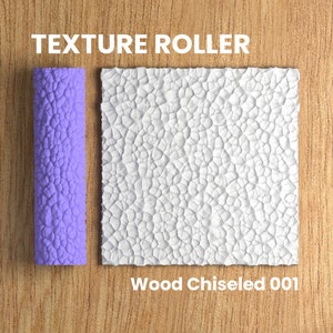 Op de afbeelding: Paarse textuurroller met een houtbeitelpatroon. De roller wordt gebruikt om een ​​getextureerd oppervlak op muren of andere oppervlakken te creëren. De tekst "Wood Chiseled 001" staat onder het getextureerde oppervlak.