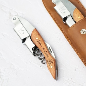 May include: Two personalised wine bottle openers with wooden handles and leather sheaths. One sheath is engraved with "R/M" and the other is engraved with "Dave & Julie Est. 2023".