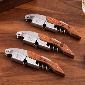 May include: Three stainless steel wine openers with wooden handles. Each opener features a metal corkscrew, a foil cutter, and a lever mechanism with the word PUSH and an arrow engraved. The wooden handles are personalised with the names Vlad, Alex Lopez, and Jackson.