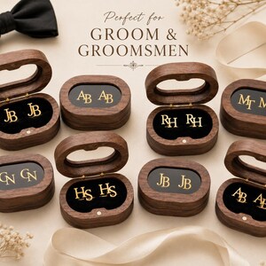 Op de afbeelding: Een verzameling houten oorbellenboxen, elk met gouden initialen oorbellen. De dozen zijn open en dicht, met een zwart interieur. Een zwarte vlinderdas staat op de achtergrond, met de tekst "Perfect for GROOM & GROOMSMEN".