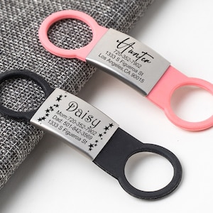 May include: Two personalized pet ID tags with black and pink silicone rings. The black tag has the name "Daisy" and phone numbers for mom and dad, along with the address "1333 S Figueroa St". The pink tag has the name "Hunter" and the address "1333 S Figueroa St, Los Angeles, CA 90015" and the phone number "720-352-7902".