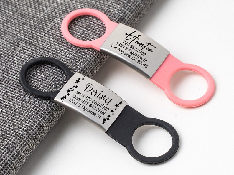 May include: Two personalized pet ID tags with black and pink silicone rings. The black tag has the name "Daisy" and phone numbers for mom and dad, along with the address "1333 S Figueroa St". The pink tag has the name "Hunter" and the address "1333 S Figueroa St, Los Angeles, CA 90015" and the phone number "720-352-7902".