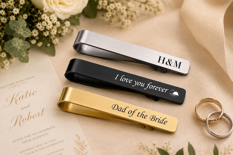 May include: Three metal tie clips in silver, black, and gold tones. The silver clip is engraved with H&M, the black clip features the text I love you forever with a sun icon, and the gold clip is engraved with the text Dad of the Bride.