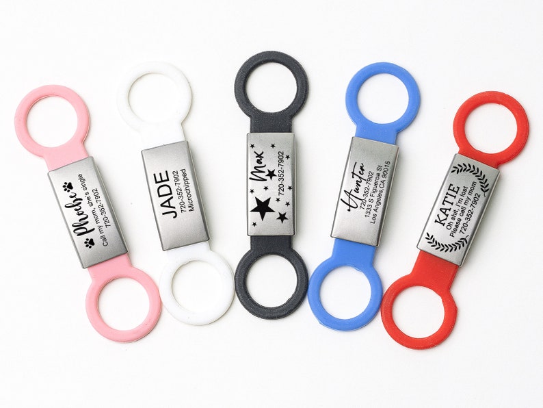K&ouml;nnte beinhalten: F&uuml;nf personalisierte Haustier-ID-Tags mit verschiedenen Namen und Telefonnummern. Die Tags sind an bunten Silikonringen befestigt.