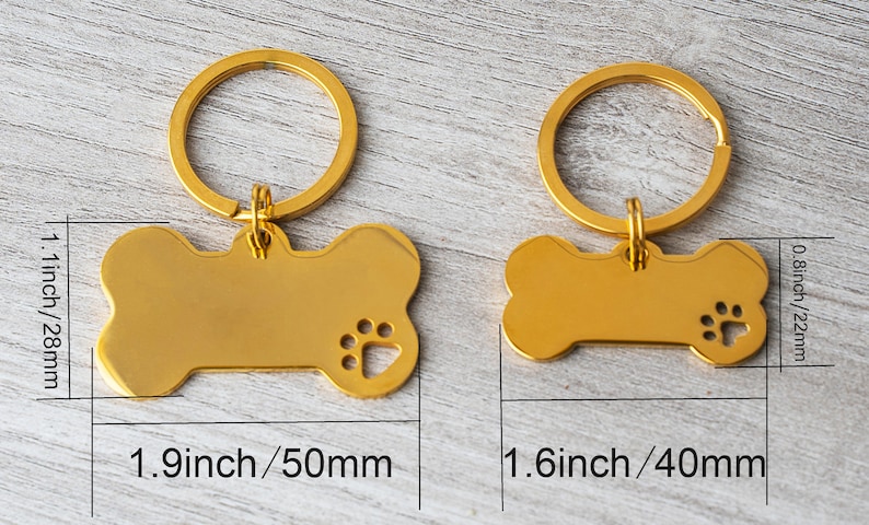May include: Two gold-colored dog bone-shaped pet ID tags with key rings. The larger tag is 1.9 inches (50mm) long and 1.1 inches (28mm) wide, with a paw print cutout. The smaller tag is 1.6 inches (40mm) long and 0.8 inches (22mm) wide.