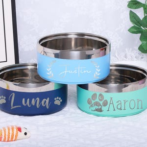 K&ouml;nnte beinhalten: Drei personalisierte Edelstahl-Futternapf f&uuml;r Haustiere. Die N&auml;pfe sind blau, t&uuml;rkis und hellblau. Die Namen sind "Luna", "Aaron" und "Justin".