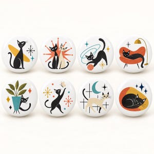 Puede incluir: Un juego de ocho botones redondos blancos con diversas ilustraciones de gatos. Los diseños incluyen gatos sentados, jugando con lana, descansando en sillas, junto a plantas, persiguiendo mariposas y durmiendo bajo estrellas y lunas.