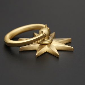 May include: A gold-toned metal door pull with a star-shaped base and a ring handle.