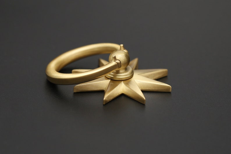 May include: A gold-toned metal door pull with a star-shaped base and a ring handle.