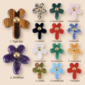 May include: A collection of thirteen flower-shaped buttons made from various stones and minerals, each featuring a central gold-toned metal stud. The set includes Tiger Eye, Amethyst, Dalmatian, Colourful agate, Rose Quartz, Obsidian, Red jasper, Blue spot, Clear Quartz, Aventurine, Yellow stone, Unakite, and Synthetic Opal.