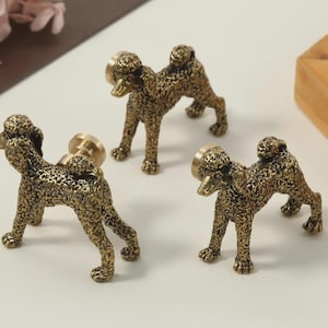 May include: Three bronze-colored poodle-shaped cabinet knobs. Each knob features a detailed poodle figure with a round base for mounting. The knobs are made of metal and have a vintage or antique appearance, suitable for furniture or decor.