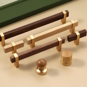 Könnte beinhalten: Eine Sammlung von Holzmöbelbeschlägen, darunter Griffe und Knöpfe. Die rechteckigen Griffe haben Messingakzente, und die Knöpfe sind rund. Die Holzfarben variieren von hell- bis dunkelbraun. Die Griffe sind ca. 15 cm lang.