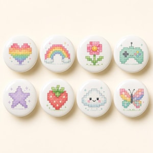 May include: A set of eight circular white buttons featuring pixel art designs including a rainbow heart, a rainbow arch, a pink flower, a green game controller, a purple star, a red strawberry, a smiling cloud, and a colorful butterfly.