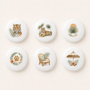 Peut inclure: Un ensemble de six boutons ronds blancs illustrés avec un visage de tigre, un tigre allongé, une feuille de palmier avec un soleil, une empreinte de patte de tigre entourée de fleurs, un fauteuil en rotin et un parasol avec des fleurs.