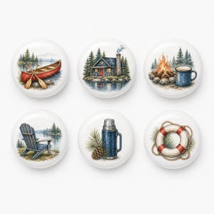 May include: A set of six round white ceramic knobs featuring illustrations of outdoor themes including a red canoe, a blue cabin, a campfire with a mug, a wooden chair by a lake, a blue thermos with a pinecone, and a red and white life preserver.