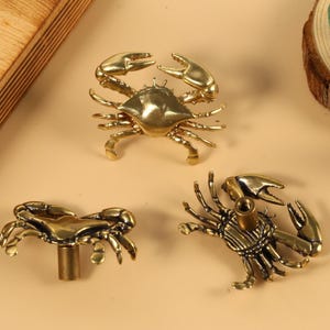 Op de afbeelding: Drie gouden metalen ladegrepen in de vorm van krabben en kreeften. De grepen hebben een gedetailleerd ontwerp en zijn perfect om elke woning een maritieme touch te geven.