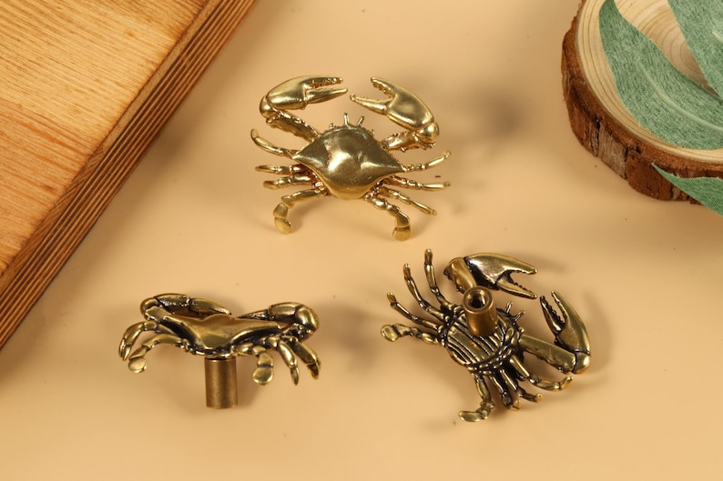 Op de afbeelding: Drie gouden metalen ladegrepen in de vorm van krabben en kreeften. De grepen hebben een gedetailleerd ontwerp en zijn perfect om elke woning een maritieme touch te geven.