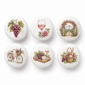 Puede incluir: Un juego de seis pomos redondos de cerámica blanca, cada uno con una ilustración diferente: un racimo de uvas moradas, una copa de vino con una rosa, una puerta de jardín, una bicicleta con una cesta de vino, queso con uvas y una cesta.