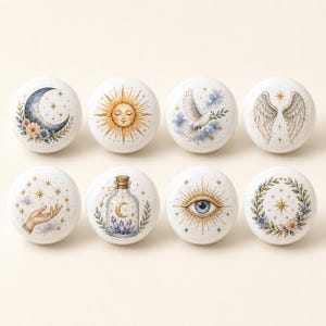 Könnte beinhalten: Ein Set aus acht runden, weißen Keramikknöpfen, die jeweils mit einer individuellen Illustration versehen sind. Die Motive zeigen eine Mondsichel mit Blumen, eine Sonne, eine fliegende Taube, Engelsflügel, eine Hand, eine Flasche, ein Auge und einen Kranz.