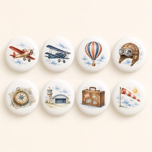 May include: A set of eight round white ceramic knobs featuring watercolour illustrations of aviation themes including a red aeroplane, blue biplane, hot air balloon, aviator helmet, compass on a map, airport hangar, brown suitcase, and windsock.