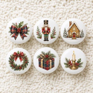 Puede incluir: Un juego de seis pomos redondos de cerámica blanca con ilustraciones navideñas. Los diseños incluyen un lazo de cuadros, un cascanueces, una casa de jengibre, una corona, un regalo envuelto en cuadros y una vela encendida en un candelabro.