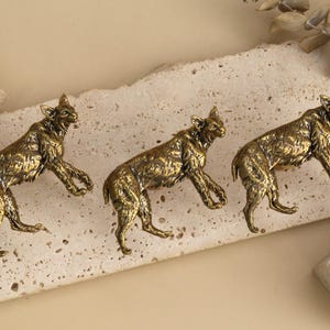 May include: Three metallic gold-toned cabinet knobs shaped like bobcats in a leaping pose. Each knob features detailed fur texture and pointed ears, designed to be mounted onto furniture surfaces with a sturdy, realistic animal silhouette.