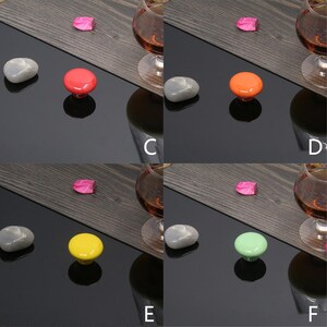 K&ouml;nnte beinhalten: Eine Auswahl an farbenfrohen Schrankkn&ouml;pfen in verschiedenen Farben, darunter Wei&szlig;, Schwarz, Rot, Orange, Gelb, Gr&uuml;n und Blau. Jeder Knopf ist rund und hat einen Stiel zur Befestigung. Der wei&szlig;e Knopf ist mit den Ma&szlig;en 32*24mm beschriftet.