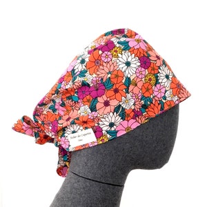 Peut inclure: Un bonnet de scrub chirurgical à imprimé floral coloré avec une cravate. Le bonnet est en tissu et porte une étiquette indiquant "Atelier des Coquettes".