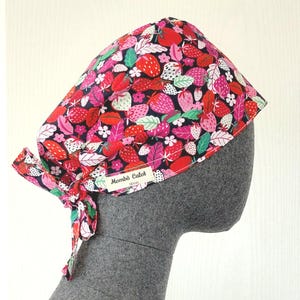 Peut inclure: Une charlotte chirurgicale ornée d'un motif vibrant de fraises rouges, roses et blanches avec des feuilles vertes sur fond noir. Le bonnet comprend un lien à nouer à l'arrière et une étiquette en tissu blanc avec le texte Mombô Calot.