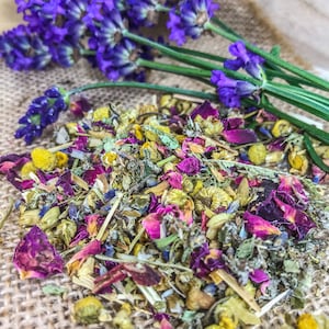 May include: A close-up of a blend of dried herbs and flowers, including lavender, chamomile, and rose petals. The mixture is a light brown colour with hints of purple, yellow, and pink.