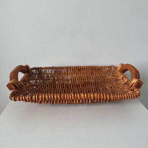 May include: A rectangular woven wicker tray with two wooden handles. The tray is brown and has a natural woven pattern.
