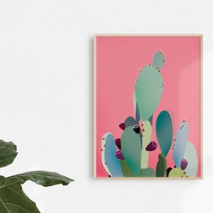 Puede incluir: Una impresión enmarcada de una ilustración estilizada de una planta de cactus con almohadillas verdes y azules y frutos morados sobre un fondo rosa.