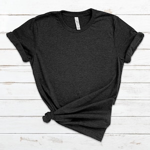 May include: Dark grey t-shirt with a crew neck and short sleeves. The shirt is knotted at the bottom. The shirt is made of a soft material and is displayed on a white wooden surface.