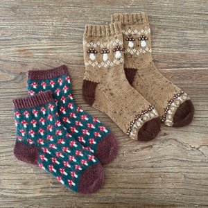 May include: Two pairs of socks with mushroom patterns. One pair is brown with white mushrooms and the other pair is green with red mushrooms.